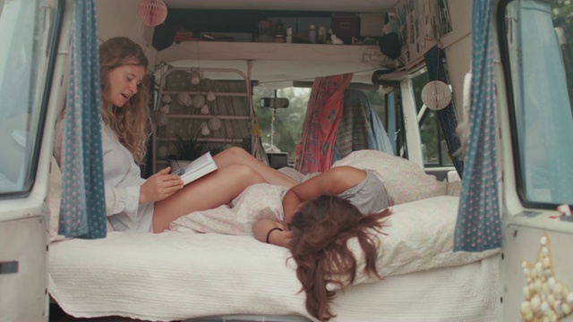 两个漂亮的女人在一辆面包车/露营的床上看书视频素材