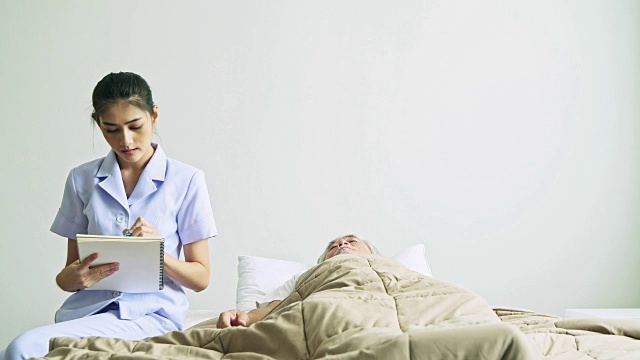 躺在床上的老男人和护士进来检查他的健康状况。年老的亚洲男人和美丽的亚洲护士女人在卧室。高级家居服务理念。视频下载