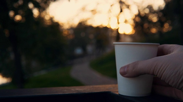 男人的手与一杯热咖啡在日落公园的背景。视频素材