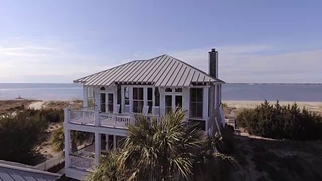 无人机在一个阳光明媚的夏日，从空中飞过豪华的两层海滨秃头岛海滩房子，可以看到远处的海洋。视频下载