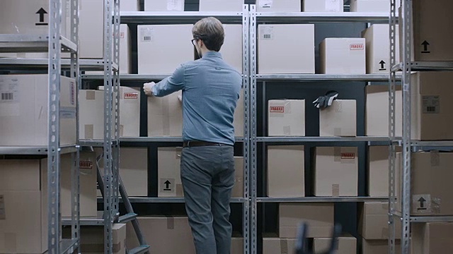 男性和女性仓库库存经理交谈，解决问题，使用个人电脑和检查库存。在背景的货架上满是纸箱包装。视频素材