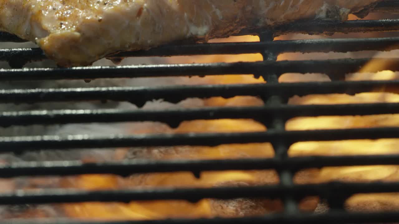摄像机慢慢地揭示了在烧烤架上燃烧的炭火上烹饪的鲑鱼牛排视频下载