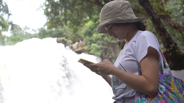 一名亚洲女性在瀑布附近使用智能手机视频素材
