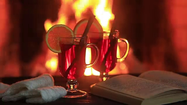 木桌子上放着热红酒和一本书。壁炉与温暖的火的背景视频素材