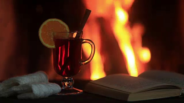 木桌子上放着热红酒和一本书。壁炉与温暖的火的背景视频素材