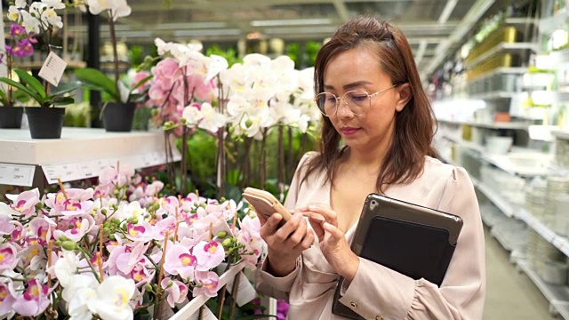 商业女性在花店检查库存的数字平板电脑和使用手机视频素材