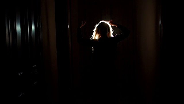 在黑暗的长廊里，一个金发女孩的剪影在风中飘扬视频素材