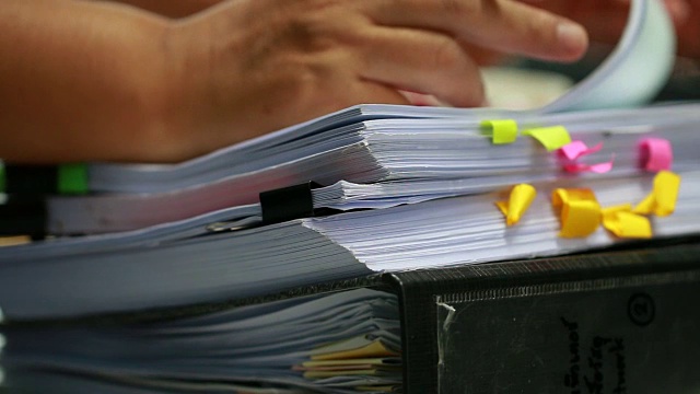 会计计划预算概念:商务女性办公室工作中整理文件未完成的堆文件用纸，用笔夹在繁忙的办公桌上视频下载