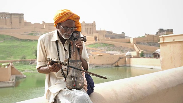 在拉贾斯坦邦的湖边，一位年长的街头男音乐家在弹奏印度古典乐器视频下载