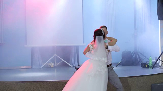 快乐的新婚夫妇在聚光灯下的餐厅跳第一支舞。视频素材