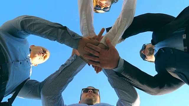 年轻的商业伙伴站在户外，双手叠在一起。成功的同事把他们的手臂放在中央，举起他们的蓝天。团结协作的理念。低角度的观点视频下载