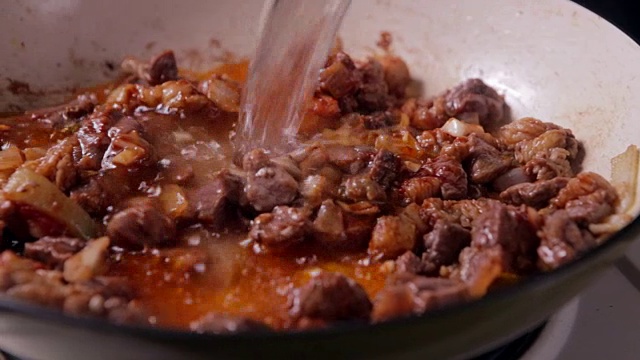 将水倒入煎锅中，加入牛肉和洋葱。准备食物。视频下载