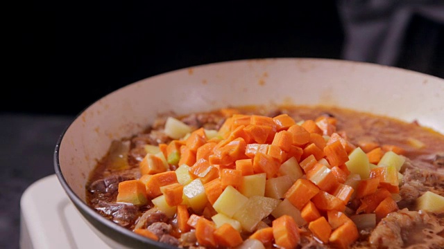 将切碎的胡萝卜与牛肉和土豆一起放入煎锅中。准备食物。视频下载