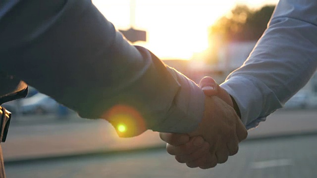 两个成功的商人在停车场的背景下互相问候的特写。日落时分，年轻的同事们在城市街道上见面握手。业务握手户外。视频素材