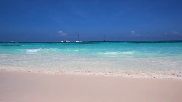 在加勒比海岛屿的白色沙滩上翻滚的波浪。地平线上的游艇视频下载
