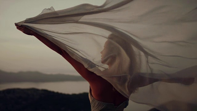 浪漫的女孩穿着长裙享受着风。站在悬崖上视频素材