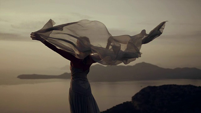 浪漫的女孩穿着长裙享受着风。站在悬崖上视频下载