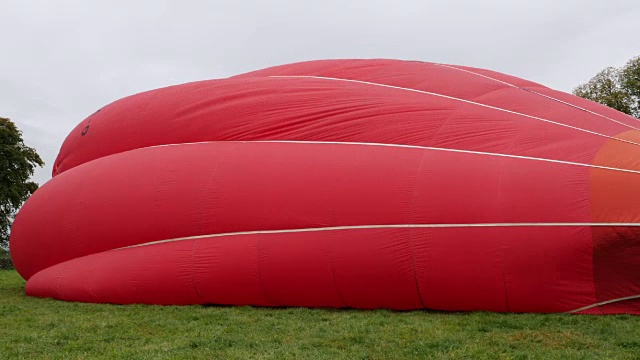 4K:热气球(红色)在地面缓慢膨胀-从侧面视频下载
