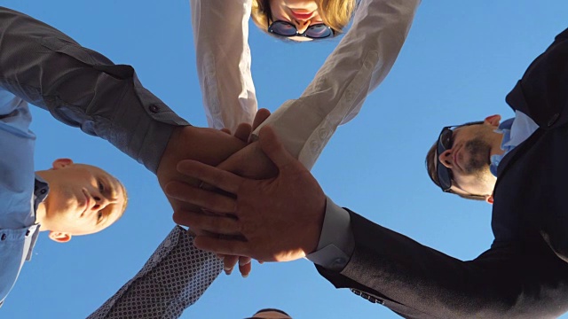 成功的商业伙伴站在一起，双手叠在蓝天的背景。年轻的同事们把手臂放在中心，象征着团结和团队合作。慢动作低角度视图视频下载