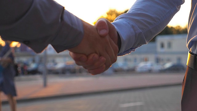 在停车场的背景下，两个成功的商人互相问候。日落时分，年轻的同事们在城市街道上见面握手。业务握手户外。慢动作视频素材