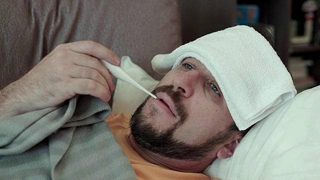 一个留着胡子的男人用医用体温计测量自己的体温。他感冒了视频下载