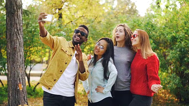 非洲裔美国学生与站在公园里的漂亮女孩自拍，用智能手机摆姿势拍照。青春与摄影理念。视频素材