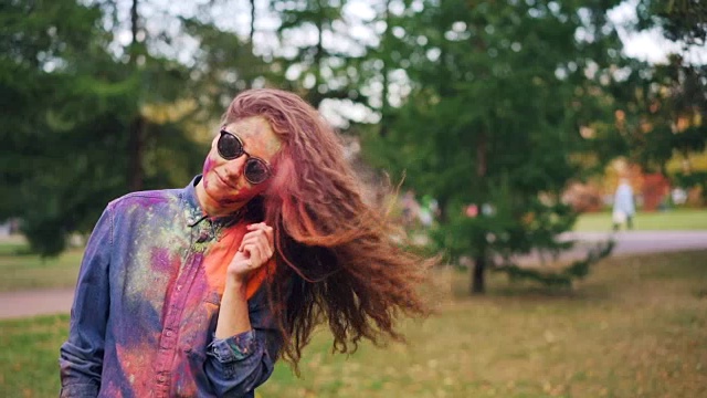 可爱的年轻女学生在胡里节抛着她涂了彩色粉的头发独自站在公园外面玩的慢动作肖像。视频下载