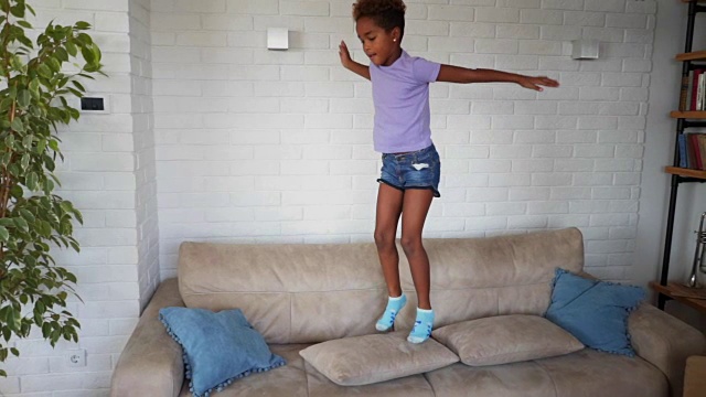 漂亮的孩子在家里的沙发上蹦蹦跳跳视频素材