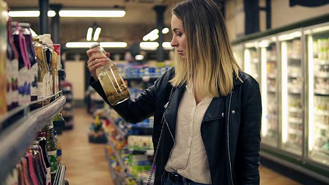 侧面的微笑女子在超市选择果汁在瓶子和把它放在篮子里。金发微笑的女人在购物中心选择产品视频素材