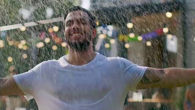 英俊健美的年轻人享受新鲜的水雨水花园水管洒水，举起手臂。肌肉男在炎热的夏天降温。视频素材