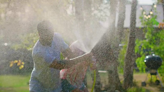 快乐的年轻夫妇在一个炎热的夏天玩水软管洒水器在花园。到处喷水，弄湿了他们。在缓慢的运动。视频素材