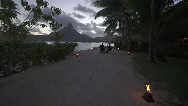 在博拉博拉的日落时分，一对男女在热带岛屿度假胜地的海滩上用餐。视频素材