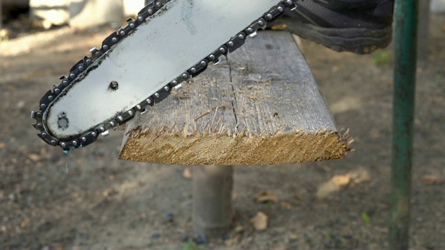 一个人用电锯锯掉一块旧木板，把脚搁在上面。视频下载