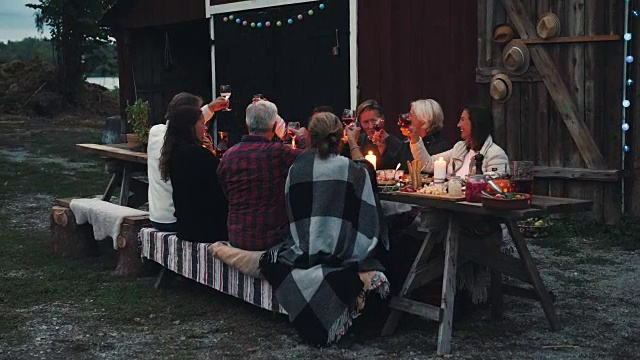 在后院的收获晚宴上，快乐的朋友们坐在餐桌前举杯互敬视频素材