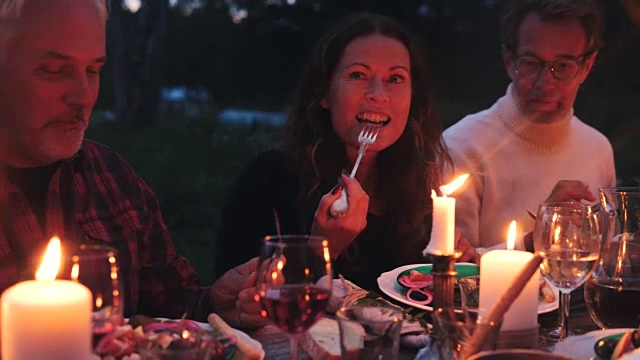 黄昏时分，在后院的收获晚宴上，成熟的女人一边和朋友聊天，一边吃饭视频素材