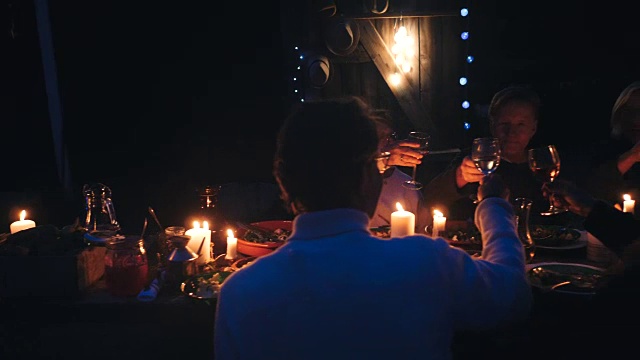 手持式拍摄的朋友敬酒在照亮的餐桌在收获晚宴在后院视频素材