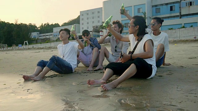 年轻的亚洲成年人坐在海滩上放松，喝着啤酒敬酒视频购买