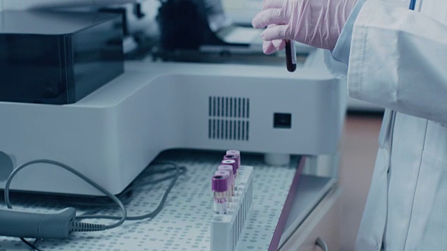 特写女研究科学家的手拿试管与血液样本，并把它放入医学分析设备。科学家在现代制药实验室工作视频素材