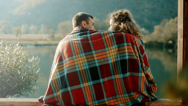 男人和女人在毯子下面坐在湖边视频素材
