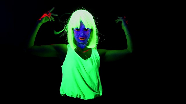 女人脸上涂着紫外线，戴着假发，穿着闪闪发光的衣服在镜头前跳舞。白人女人。。视频下载