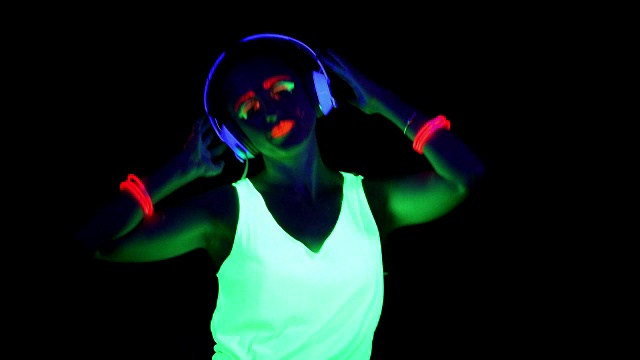 女人涂着紫外线漆，戴着发光的手镯，穿着衣服跳舞，戴着耳机听音乐。白人女人。。视频下载