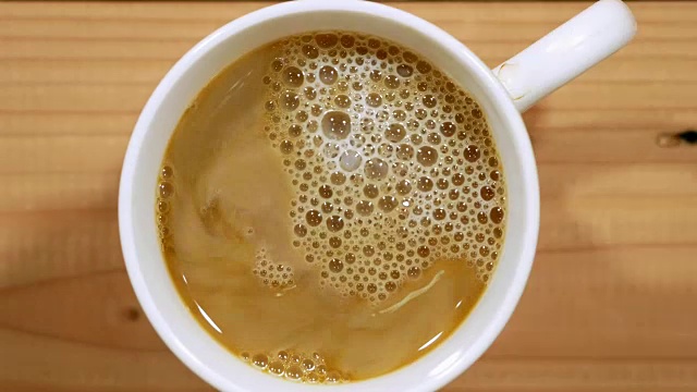 把牛奶倒进黑咖啡里，搅拌，放在木桌上拿起来视频素材