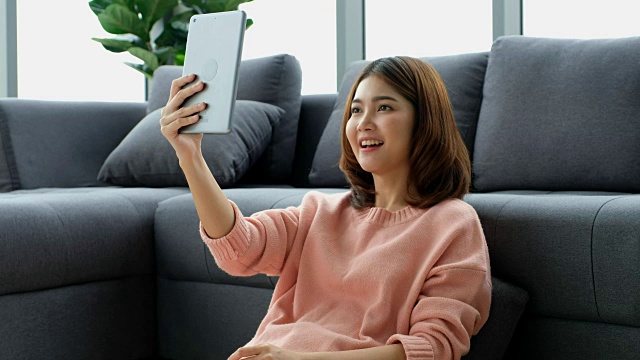 年轻的亚洲女子使用智能手机在客厅进行视频通话视频素材