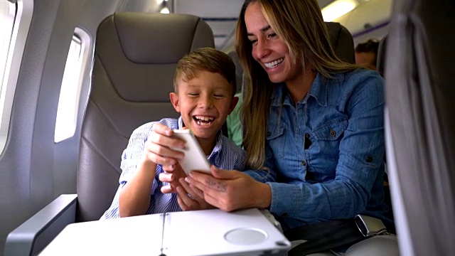 爱的妈妈和儿子在飞机上玩智能手机，都微笑着视频素材