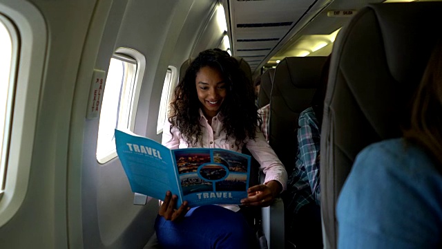 愉快的年轻黑人妇女在飞机上看旅游指南视频下载