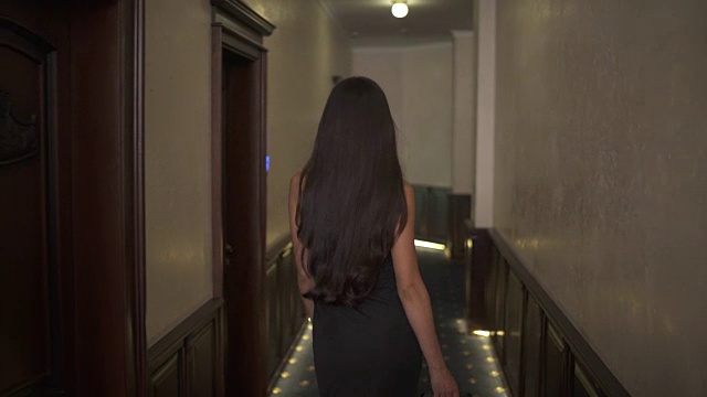 一个深褐色头发的女人沿着酒店走廊走的背影特写。长发随着她的脚步而移动视频下载