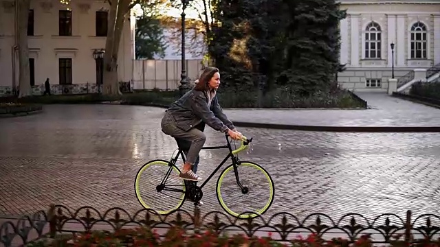 女人在城市铺好的道路上骑自行车。骑自行车的女人在早上骑车。空的城市街道与美丽的老建筑的背景视频素材