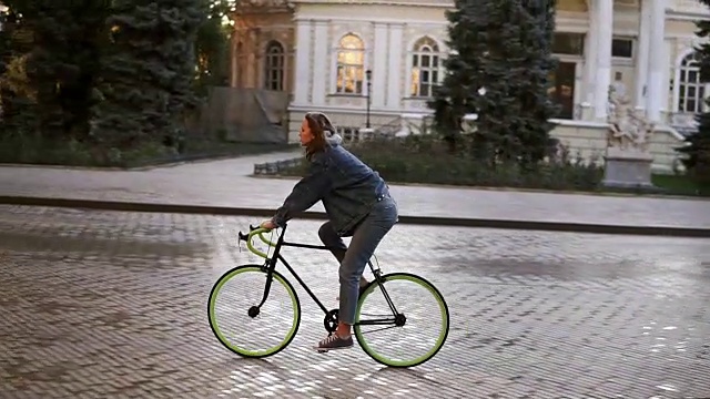 女人在城市铺好的道路上骑自行车。骑自行车的女人在早上骑车。空的城市街道与美丽的老建筑的背景。侧视图视频素材