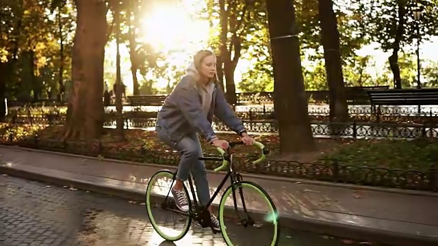 漂亮的白人女性在早上骑自行车在公园或大道。侧面的一个年轻女子骑着一辆徒步自行车，穿着运动鞋和休闲服。慢动作视频素材