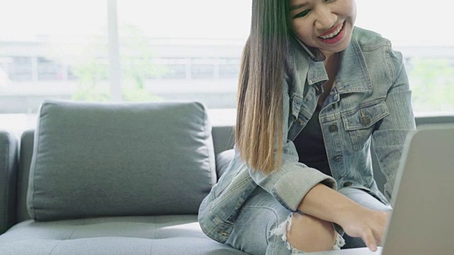 迷人的年轻亚洲女人在家里看笔记本电脑，同时通过手机与客户在自由职业者时髦的概念。视频素材